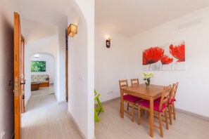 A dining area with a wooden table and chairs, a wall-mounted light fixture, and a painting of red flowers.