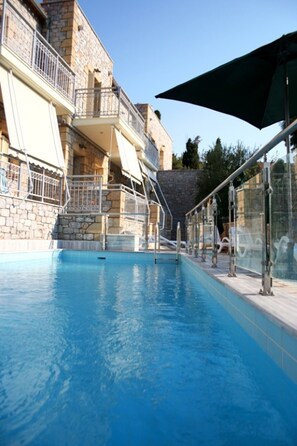 A swimming pool with a glass railing, a stone building, and a metal staircase. - Manoleas Villas - Apartment 2 (West Mani)