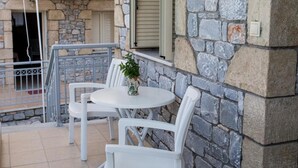 A balcony with white chairs and a small table, a stone wall, and a window with shutters. - Manoleas Villas - Apartment 3 (West Mani)