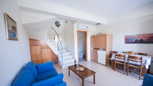 Een woonkamer met een blauwe bank, een houten salontafel en een trap die naar een keuken leidt.