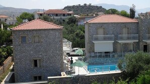 A stone building with a red-tiled roof, a pool, and a view of the surrounding area. - Manoleas Villas - Apartment 6 (West Mani)
