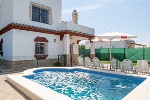 A swimming pool with a tiled edge, a covered patio area, and a building with a stone chimney.