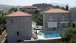 Un bâtiment en pierre avec un toit recouvert de tuiles rouges, une piscine et une vue sur un paysage vallonné.