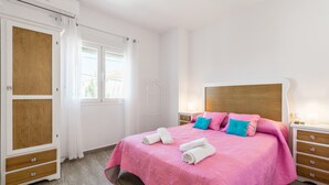 A bedroom with a bed, pillows, a nightstand, a wooden wardrobe, and a window with curtains. - Modern studio apartment - La Higuera 3 (Cadiz)
