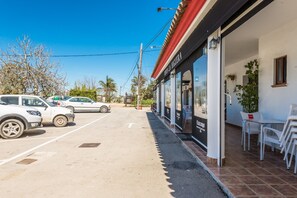 Un parking avec plusieurs voitures, un bâtiment avec un toit rouge et des sièges à l’extérieur, avec des chaises.