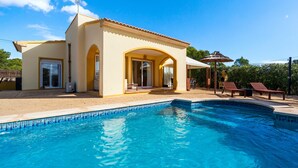 Ein Poolbereich mit einem kühlen, blauen Pool, einem Gebäude mit gelber Fassade und einer überdachten Sitzgelegenheit mit Sonnenschirmen.