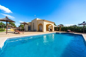 Zona de piscina con un edificio, sillas de descanso y sombrillas.