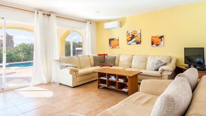 Ein Wohnzimmer mit einer Couch, einem Couchtisch und einem Fernseher. Eine Glastür führt zu einem Pool.