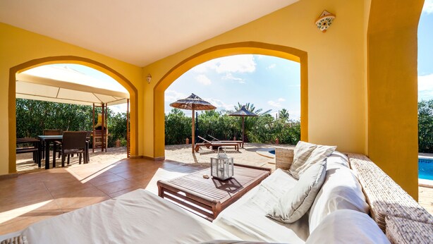 Ein sonnendurchfluteter Raum mit einem Bett, einem Holztisch und Blick auf einen Pool und Grünflächen.