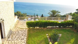 Un bâtiment en pierre doté d’un patio dallé qui mène à un balcon offrant une vue sur la mer.