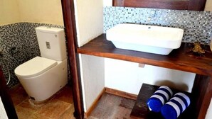 Et badeværelse med toilet, vask og en hylde med to flasker.