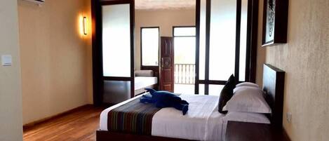 A bedroom with a wooden floor, a bed with a striped blanket, and a view of a balcony through a sliding door.
