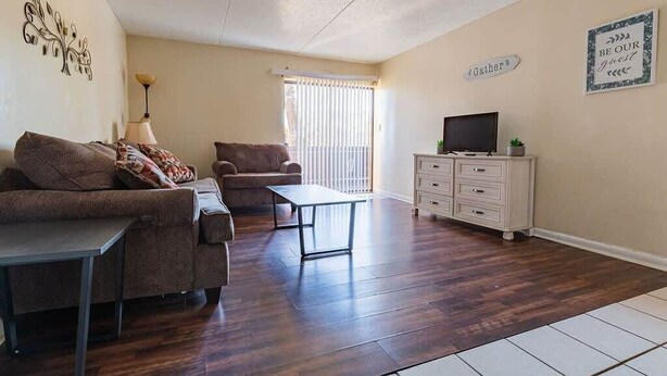 A living room with a sofa, armchair, coffee table, TV stand, and a window with blinds.