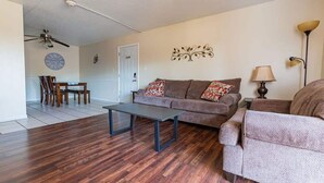 A living room with a sofa, armchair, coffee table, dining table with chairs, and a ceiling fan.