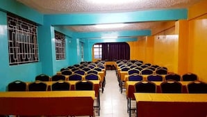 A conference room with rows of tables and chairs, a tiled floor, and a blue and yellow color scheme. - Downhill Springs Resort (Webuye)