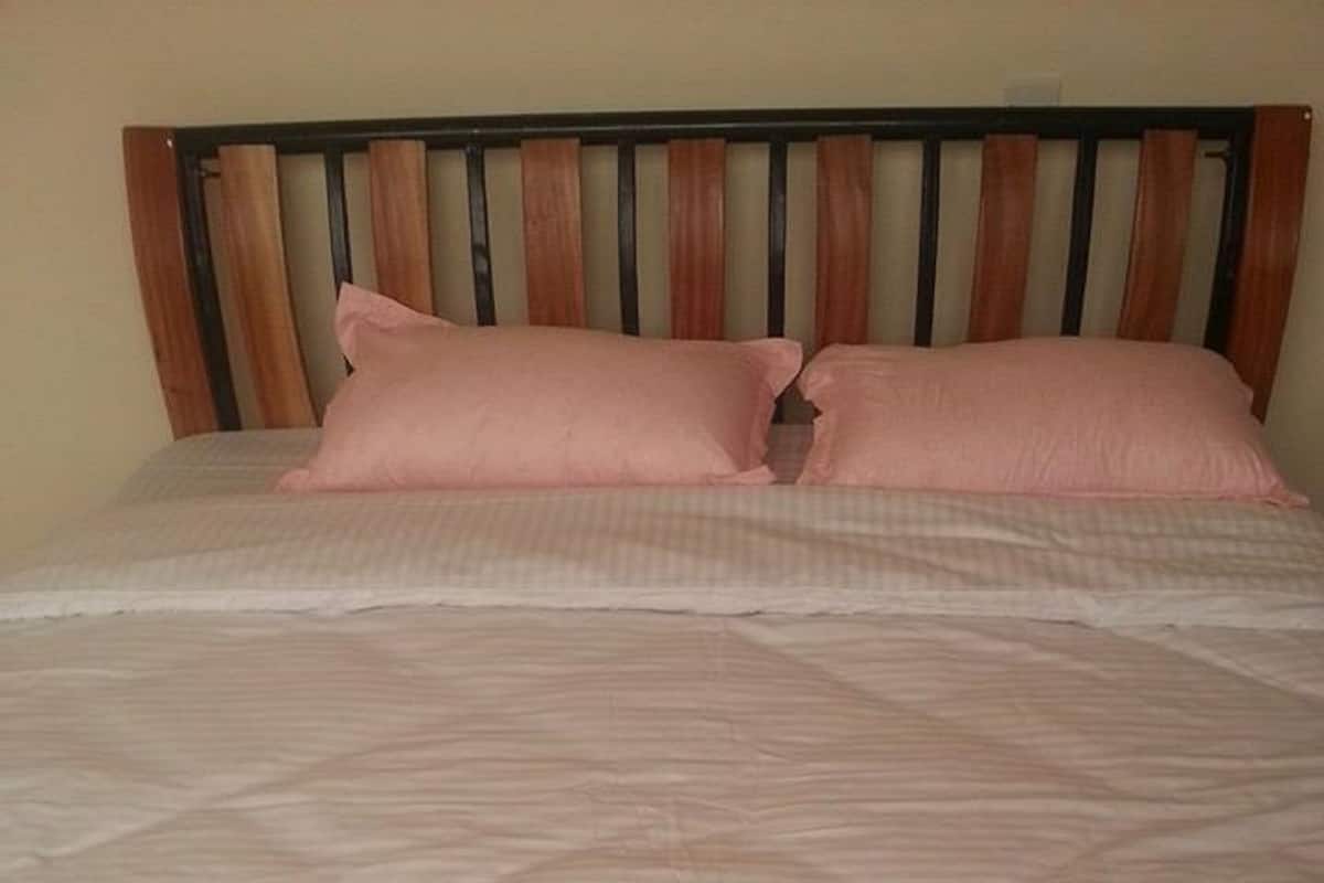 Una cama individual con cabecera de madera, colchón blanco y dos almohadas rosadas.