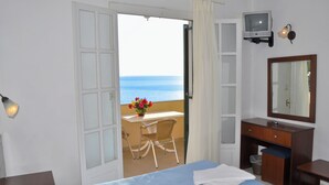 Une chambre d’hôtel comprenant un lit, un bureau avec une chaise, une télévision et un balcon avec vue sur la mer.