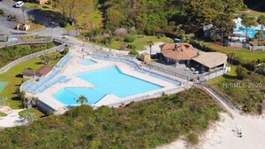 Vista aérea de un complejo turístico con una gran piscina, una zona de playa y un edificio con estructura cubierta.