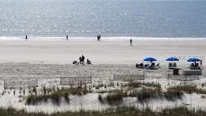 Una playa con gente caminando, algunas sombrillas y sillas.