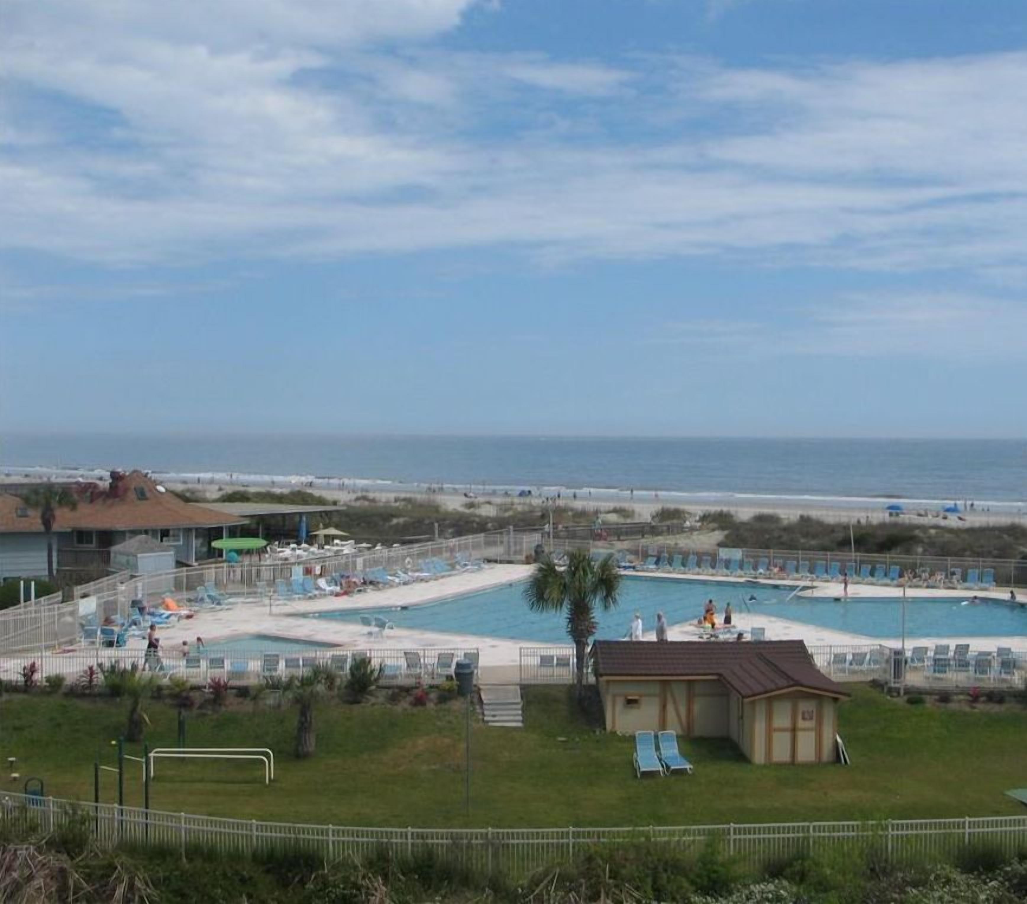 Zona de piscina con varias piscinas, sillas de descanso y un pequeño edificio, con vistas a la playa.
