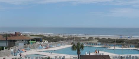 Zona de piscina con varias piscinas, sillas de descanso y un pequeño edificio, con vistas a la playa.
