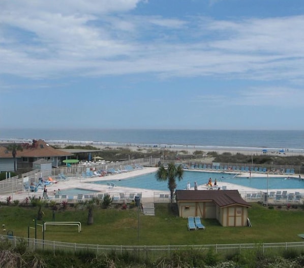 A pool area with multiple pools, lounge chairs, and a small building, overlooking a beach.