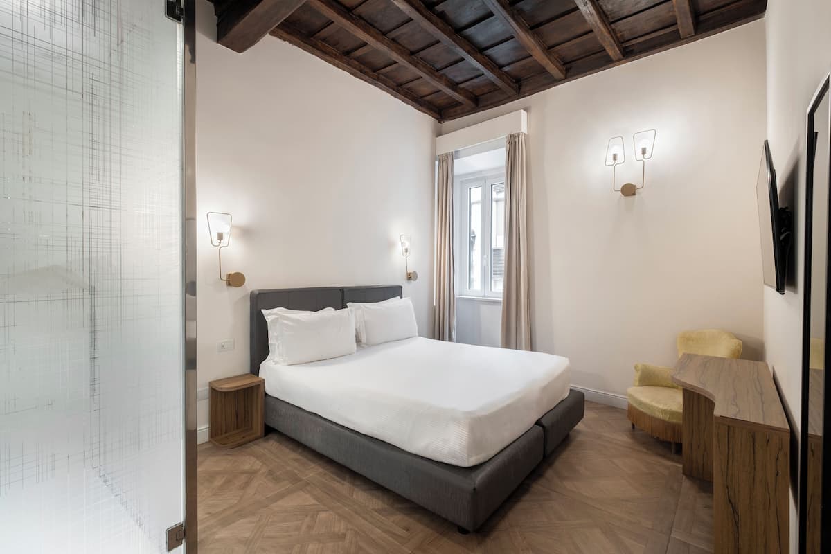 A bedroom with a bed, bedside tables, a chair, a desk, a mirror, and a window with curtains.
