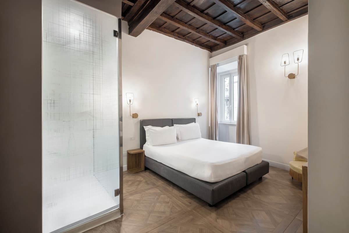 A bedroom with a bed, wooden floor, and a window with curtains.