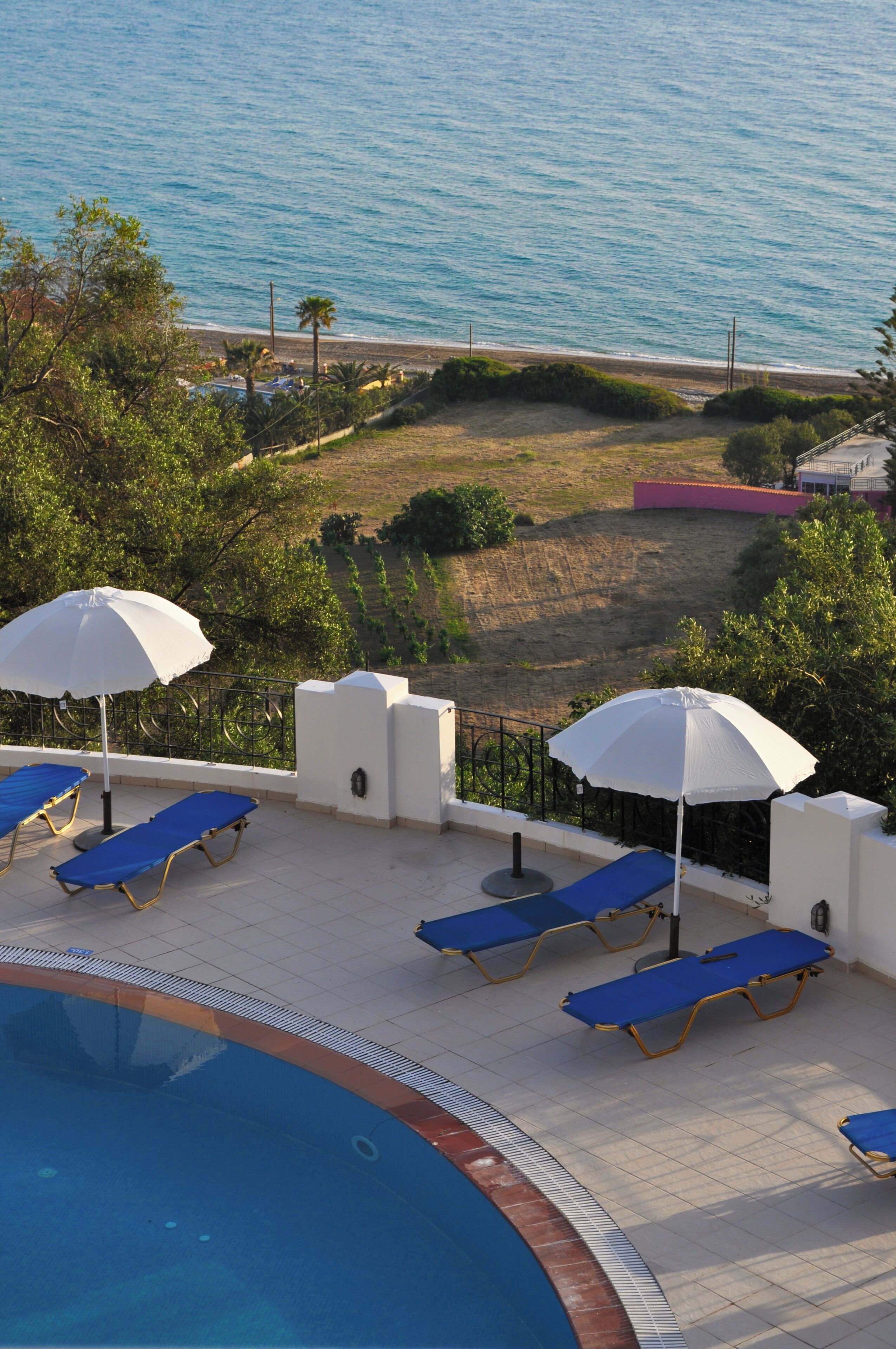 A poolside area with lounge chairs and umbrellas, overlooking a beach and ocean.