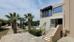 Une maison moderne à deux étages, dotée d’une piscine, d’un chemin en pierre, de palmiers et d’un escalier menant à l’étage supérieur.