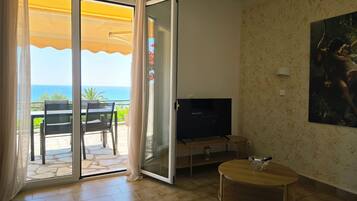 Una habitación con puerta de vidrio corrediza a un balcón, televisión, una mesita y un cuadro en la pared.