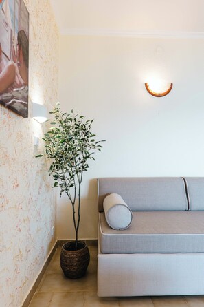 A room with a sofa, a potted plant, and a wall-mounted light fixture. - Corfu Glyfada Menigos Resort 45 (Corfu)