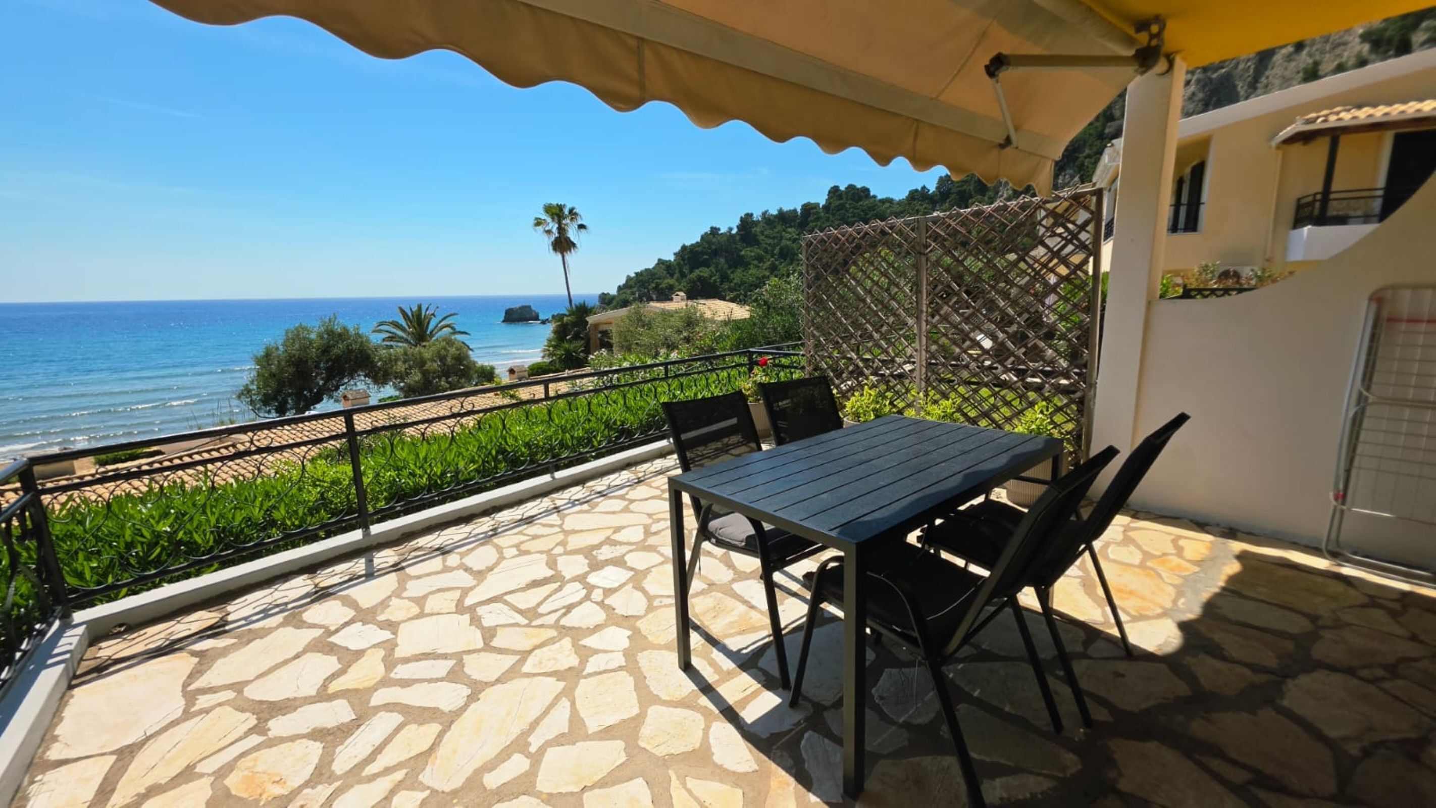 A patio with a table and chairs, a view of the sea, and a stone floor.