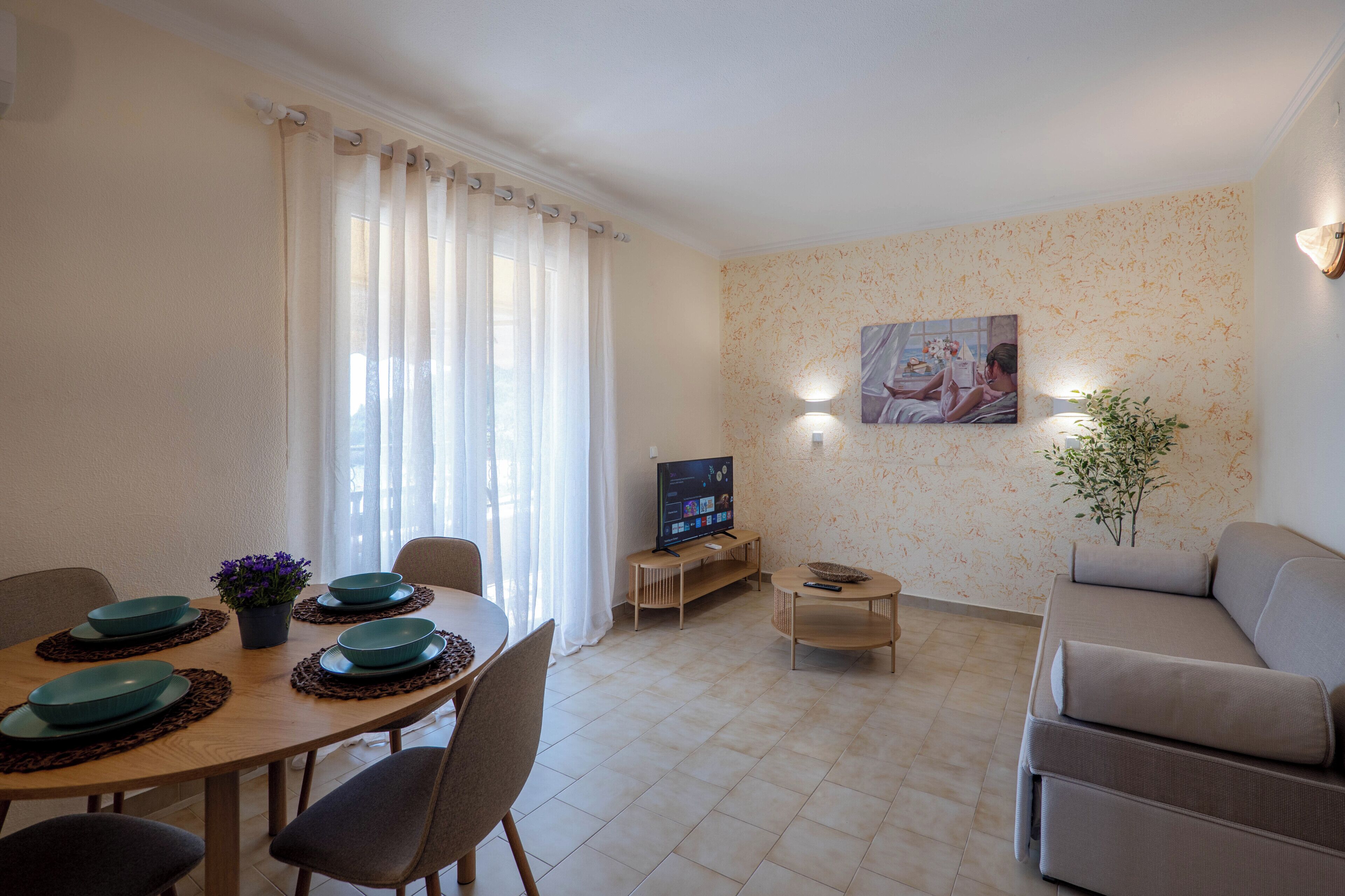 Una sala de estar con una mesa de comedor, sillas, un sofá, un televisor y una planta.