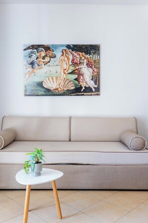 A living room with a beige sofa, a white round table with a plant, and a large painting on the wall. - Corfu Glyfada Menigos Resort 22 (Corfu)