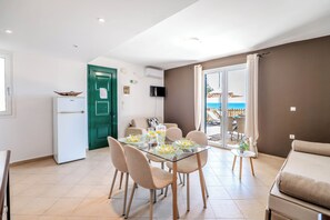 A dining area with a glass table, chairs, and a view of the sea through a sliding door. - Corfu Glyfada Menigos Resort 22 (Corfu)