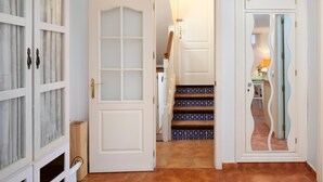 Un couloir avec une porte blanche, un escalier aux carreaux décorés et une porte miroir au motif ondulé.