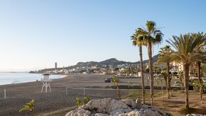 Une plage avec un poste de surveillance pour les sauveteurs, des palmiers et une montagne qui se dessine à l’horizon.