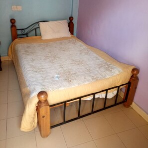 A bed with a wooden frame and a white mattress, a wooden headboard, and a plain wall with a light switch.
