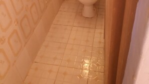 Une petite salle de bain carrelée, avec des toilettes et un meuble de rangement au-dessus.