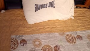 Un lit avec un oreiller portant l’inscription « FLAVOURS LODGE » et une couvre-lit à motifs.
