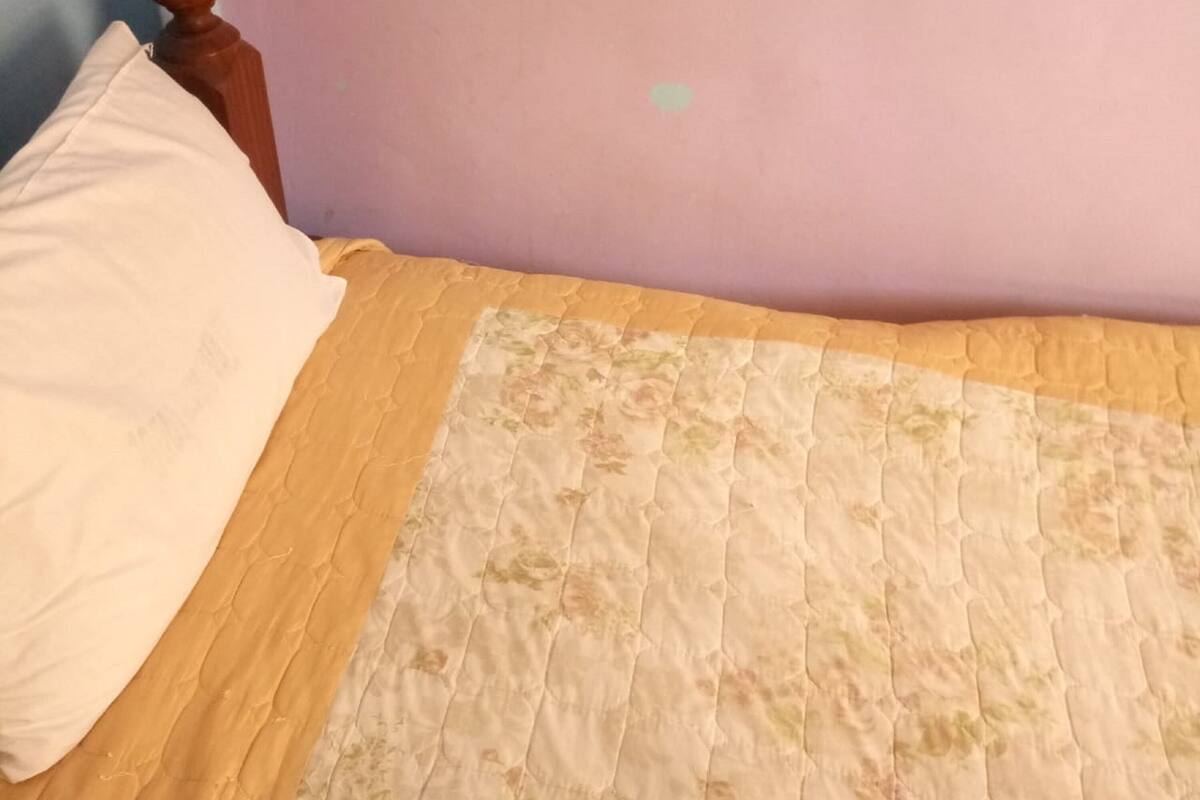Ein Bett mit einer blumigen Stegdecke, einem Holzkopfende und einer schlichten Wand.