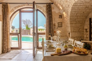 Un espace repas ouvert avec vue sur la piscine, des murs en pierre et une table dressée pour le repas.