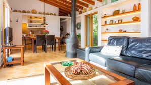 A modern living room with a leather sofa, wooden coffee table, and a dining area with chairs and a table. -  Charming Country House with Large Garden with Mountain View, Pool, Wi-Fi and Terraces (Artá)