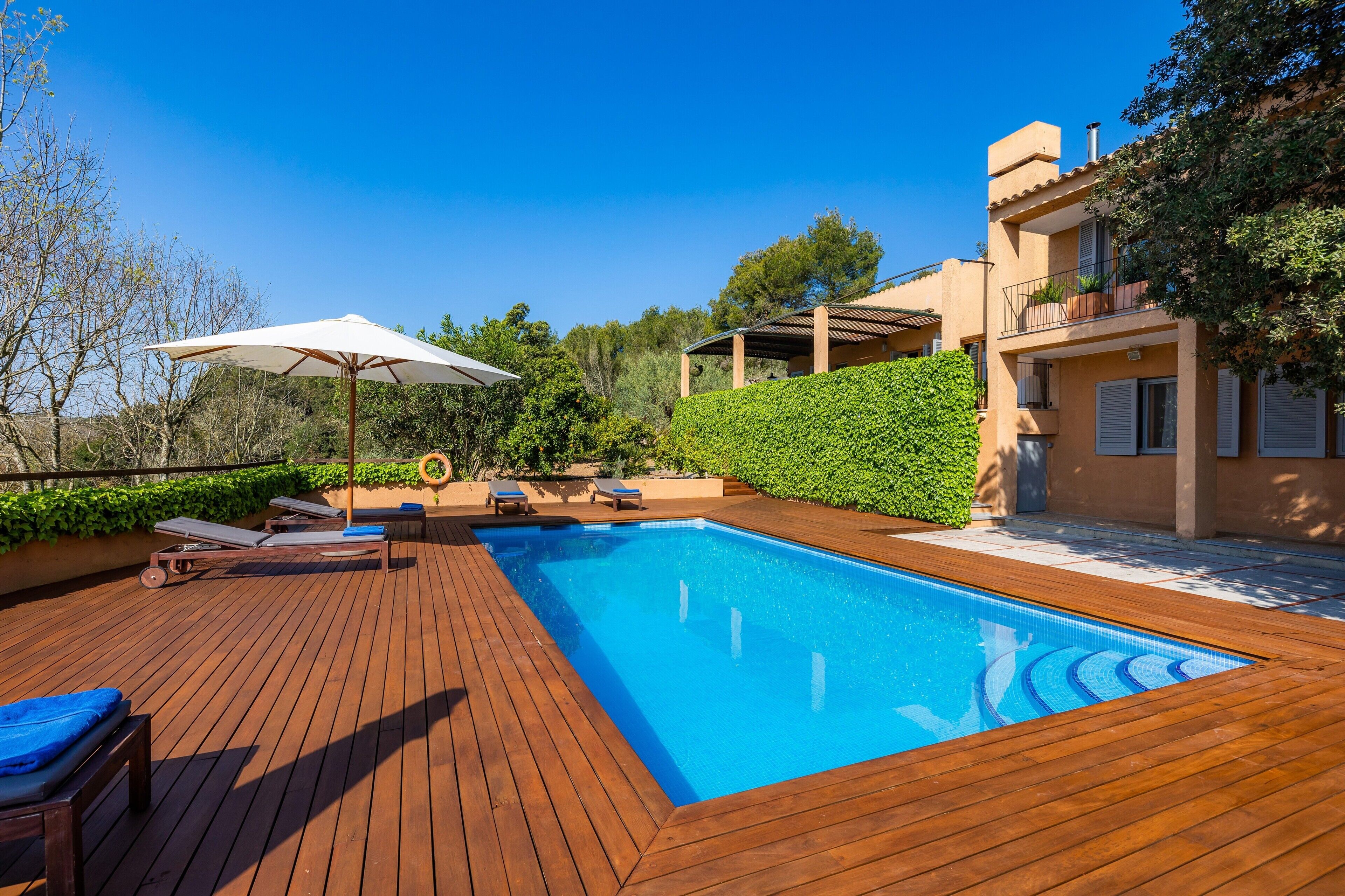 A wooden deck with a swimming pool, lounge chairs, and a pergola with an umbrella.