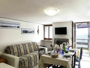 Una sala de estar con sofá, mesa de comedor lista para una comida, chimenea y televisor montado en la pared.