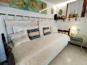 Un dormitorio con cama, almohadas, una mesita de noche, una lámpara y decoración en la pared.