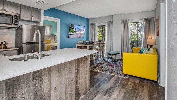 A modern kitchen with a built-in island, a dining area with a yellow sofa, and a view of the outdoors.