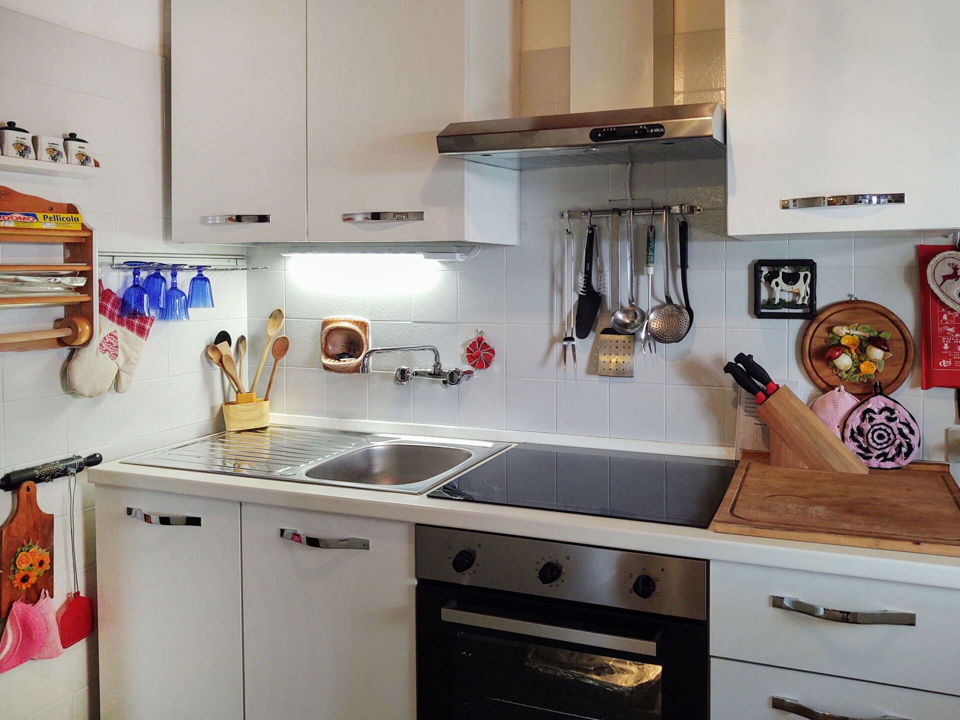 A modern kitchen with white cabinets, stainless steel appliances, and various utensils hanging on the wall.