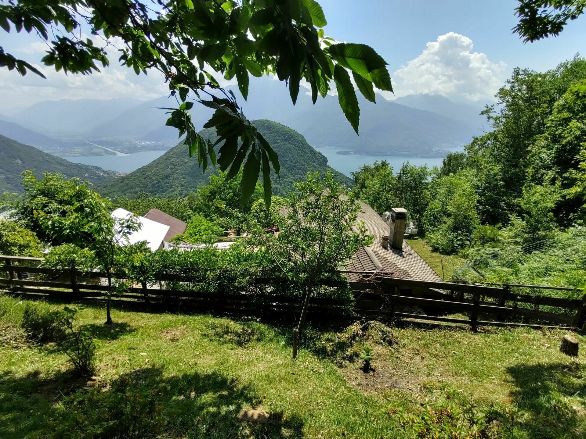Una casa rurale con tetto spiovente, immersa nel verde e con vista su un lago e le montagne.
